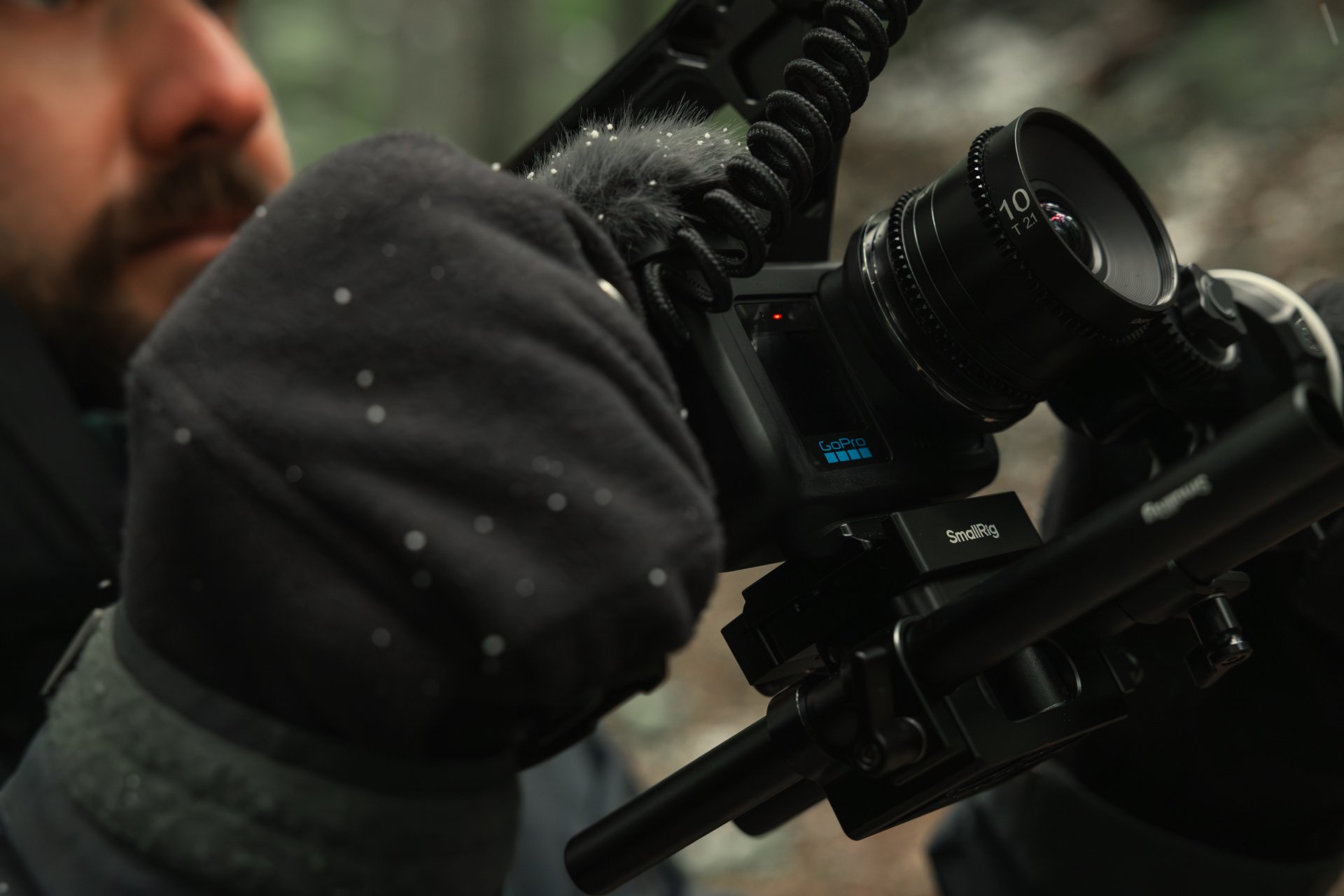 A filmmaker adjusting a rigged GoPro camera in snowy woods.