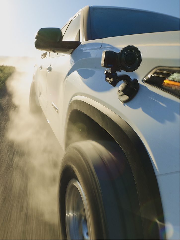 GoPro camera mounted on the side of a white truck driving on a dirt road.
