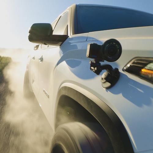 GoPro camera mounted on the side of a white truck driving on a dirt road.